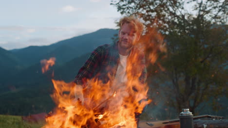 el campista hipster mira el fuego en el bosque natural. el tipo feliz se sienta en la hoguera en las montañas.