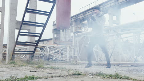 caucasian man in grey beanie and sportswear hitting a punching bag outdoors an abandoned factory on a cloudy morning