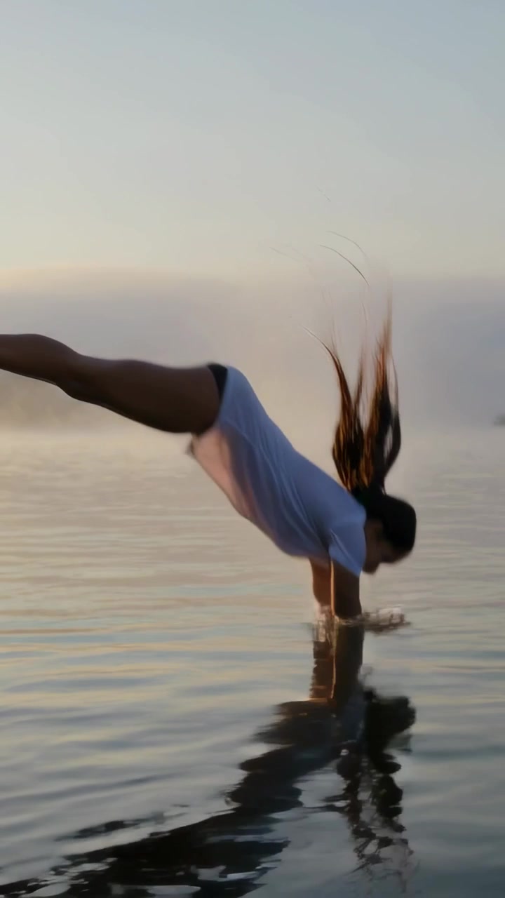 Vertical video: Running teen diving into misty lake, creating splash, wearing white tee, copy space