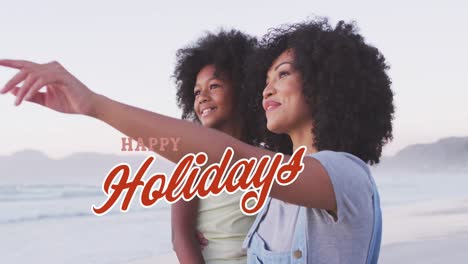 Animación-Del-Texto-De-Saludos-Navideños-Sobre-Una-Mujer-Birracial-Con-Su-Hija-En-La-Playa