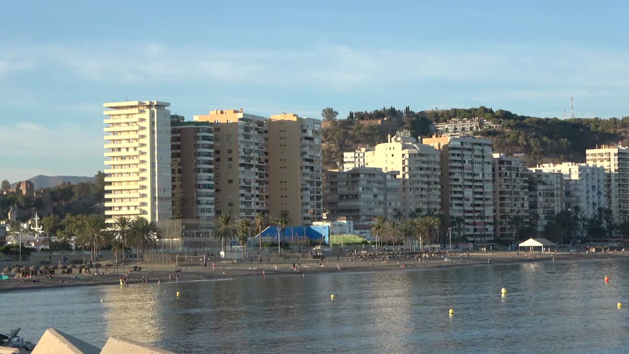 Tall beachfront buildings facing calm sea with sandy shore, gentle waves, and Mediterranean atmosphere under clear sky creating vibrant coastal city scene during daytime