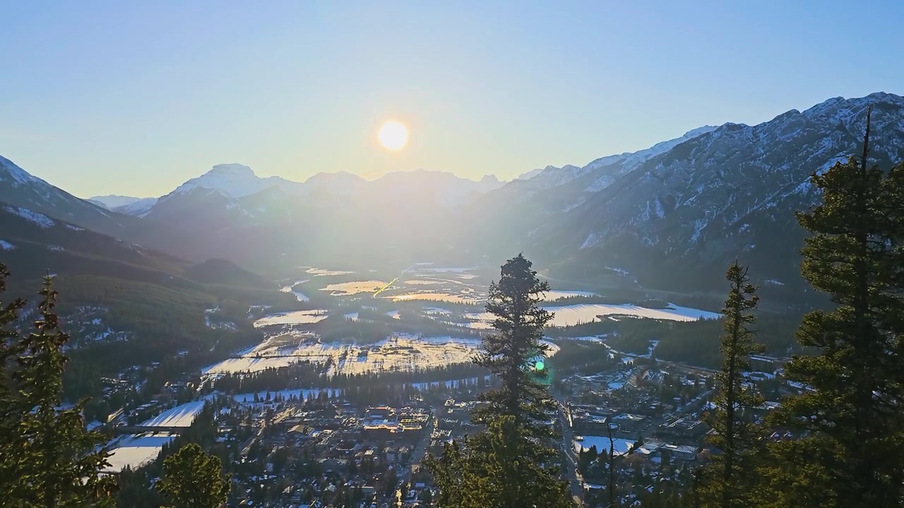 Hoàng hôn yên bình trên Dãy núi Rocky của Canada tại Vườn quốc gia Banff, với những sườn núi phủ tuyết, thung lũng rừng, các tòa nhà thị trấn, phong cảnh đóng băng, ánh nắng núi cao rực rỡ và du lịch Canada.