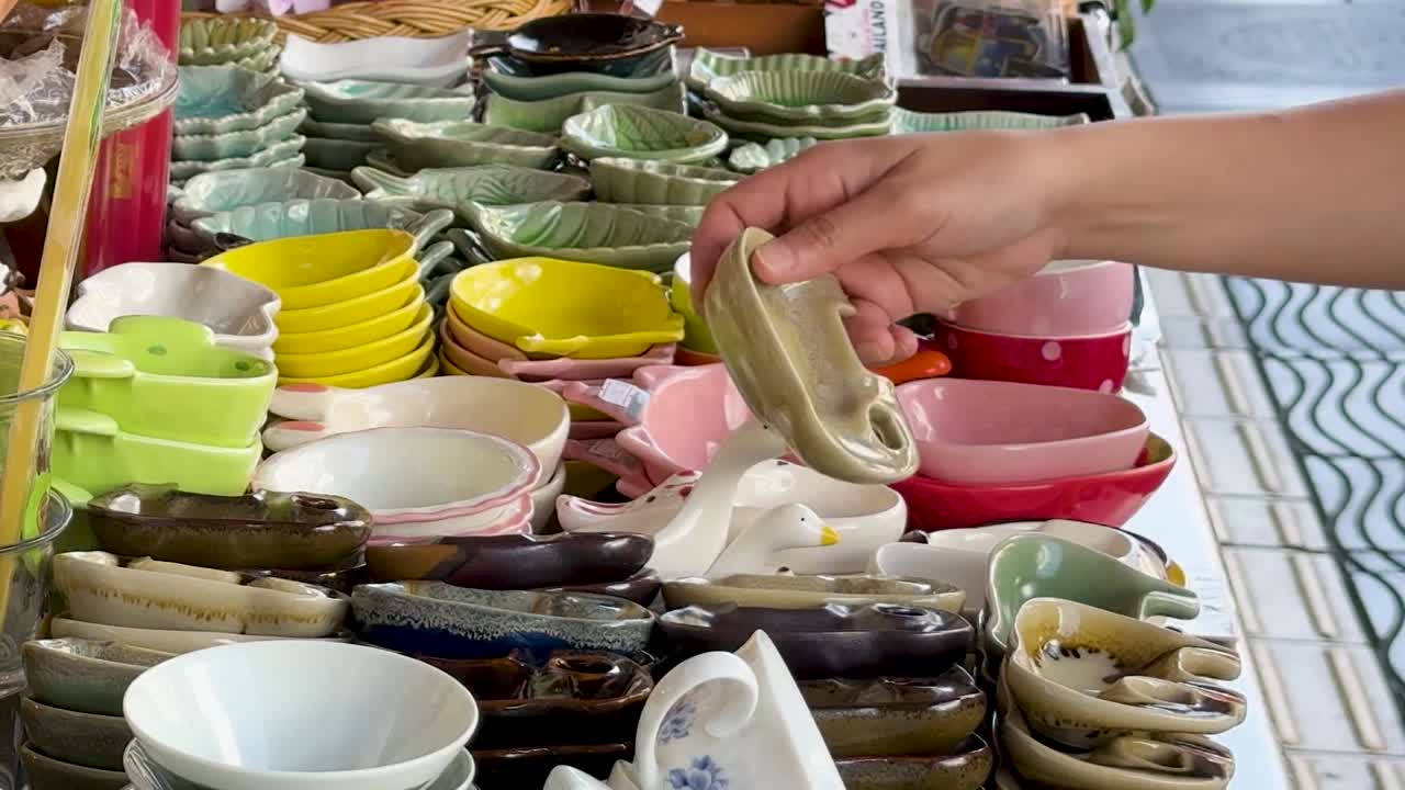 A person's hand selects and examines small, colorful handmade ceramic bowls at a market