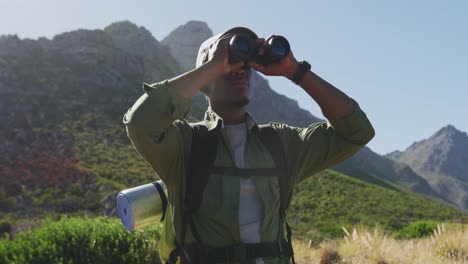 African-american-man-hiking-in-mountain-countryside-using-binoculars