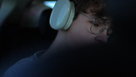 a young man with glasses and headphones in a car, intently looking at a screen