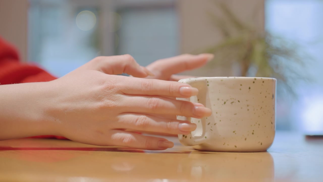 Mano di donna che tiene delicatamente una tazza di ceramica maculata su un tavolo di legno