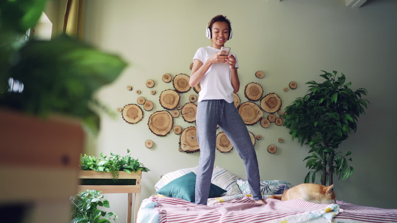 Donna felice che balla sul letto con le cuffie e il telefono