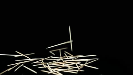 stuzzicadenti in legno chiaro cadono davanti a sfondo nero su sfondo scuro rallentatore
