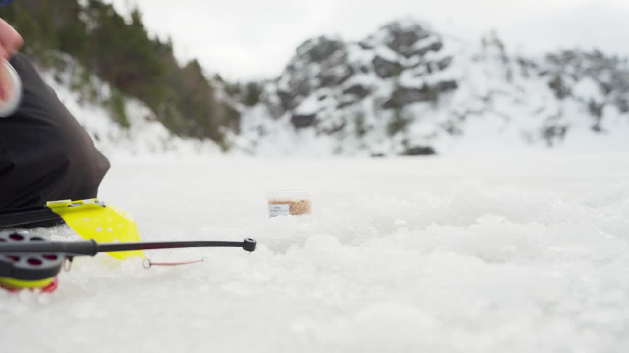 Male Fisherman Sitting With Fishing Rod On Frozen Water - Close Up