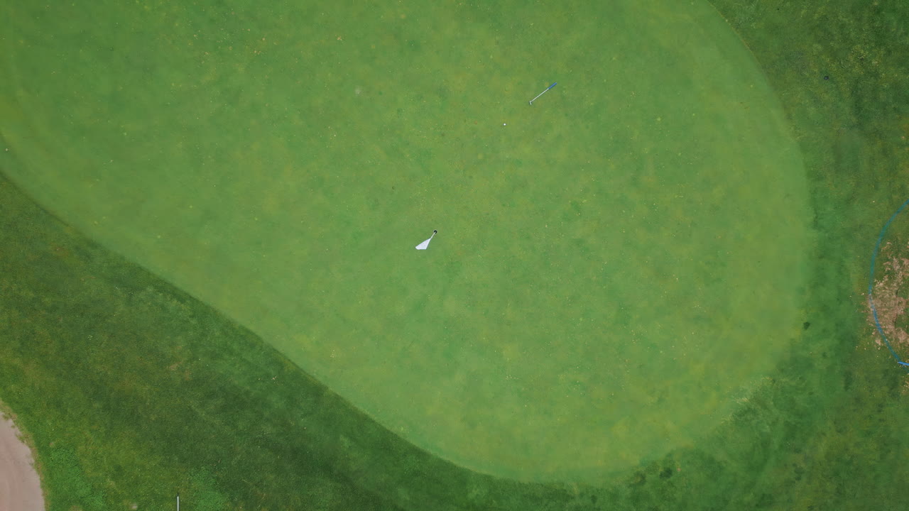 Top golf green course with solitary flag marking hole in expansive fairway.