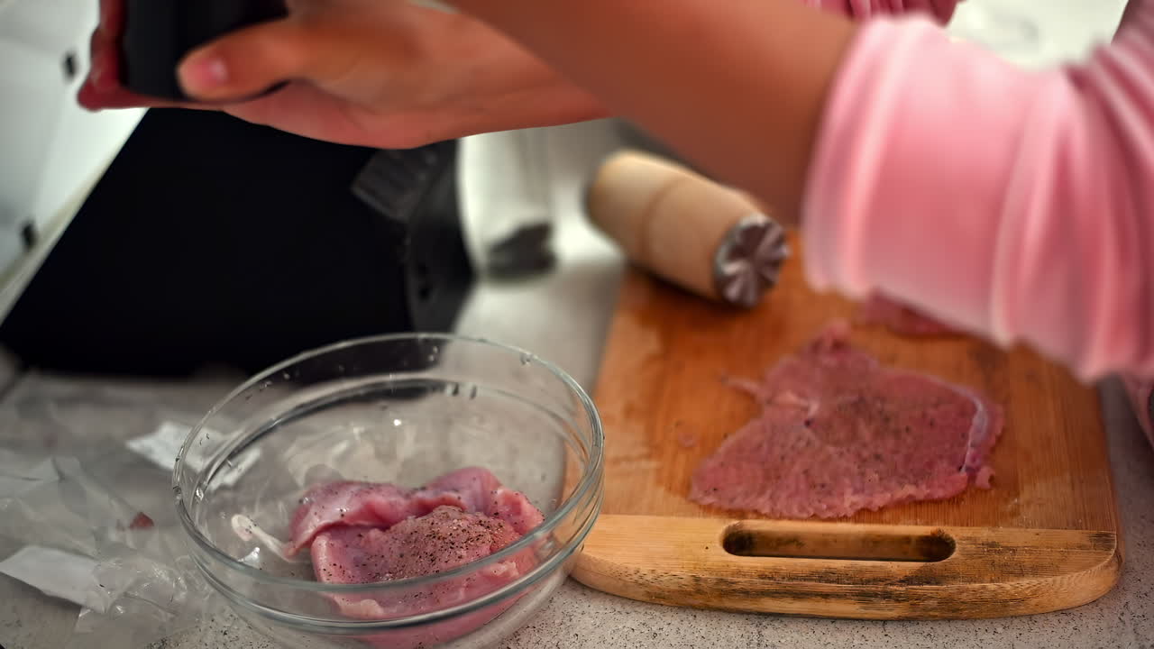 In a bright kitchen, a person seasons chicken breast with spices, then prepares it for cooking. This process showcases simple techniques for flavorful meat