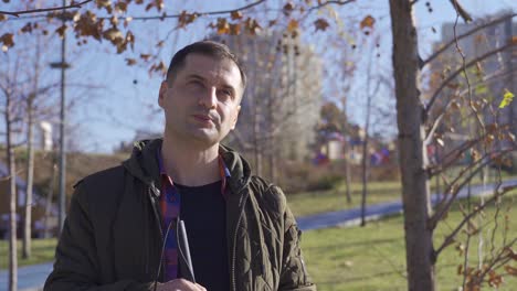 Blind-man-enjoying-the-weather-is-standing-under-the-trees-in-the-park.