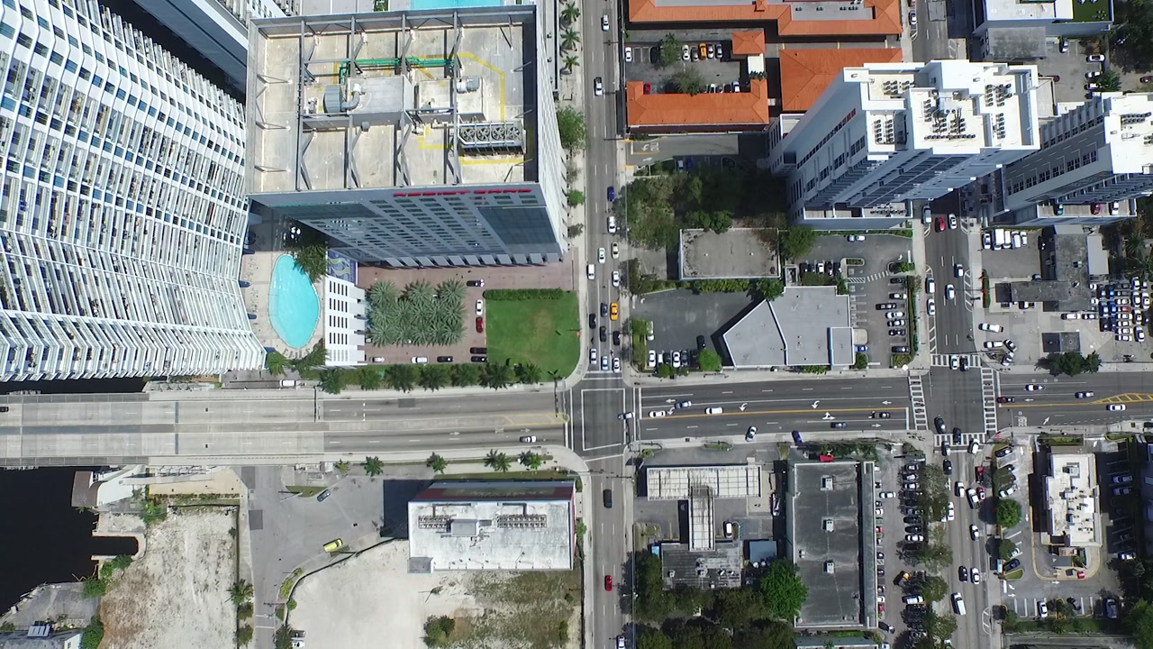 Drone top-down view of Miami city blocks with rooftops, pools and moving traffic.