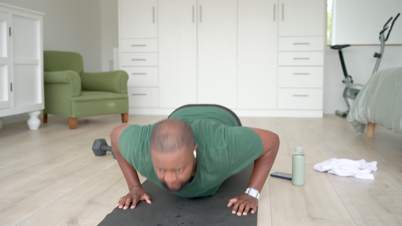 African American man starting set, lowering chest and pushing up on mat at home for strength