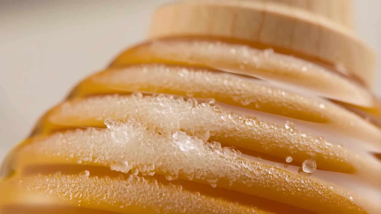 Primo piano estremo di un dosatore di miele in legno, mentre il rivestimento ambrato liscio si trasforma in cristalli di zucchero raggruppati lungo le scanalature, creando una texture ricca, un caldo luccichio e un dettaglio dolce naturale.