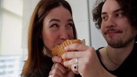 A-happy-brunette-girl-bites-a-sandwich-in-the-hands-of-her-boyfriend-which-he-wanted-to-eat-for-breakfast-in-the-morning-in-a-modern-apartment-in-the-kitchen