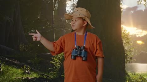 niño asiático con sombrero y binoculares sonriendo y señalando hacia un lado mientras explora la naturaleza forestal. niño investigador examina algo, concepto de aventura de turismo de viaje
