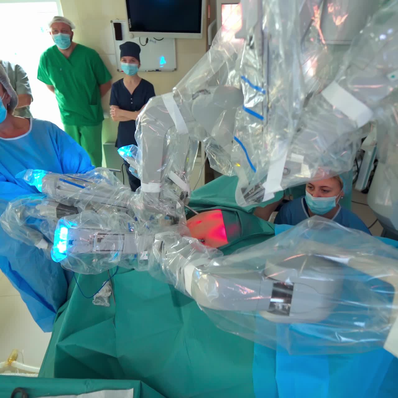 Robotic arms in patient's body at surgery. Futuristic medical robot perform minimally invasive surgery. Medical specialists observe the work of robotic equipment in operating room