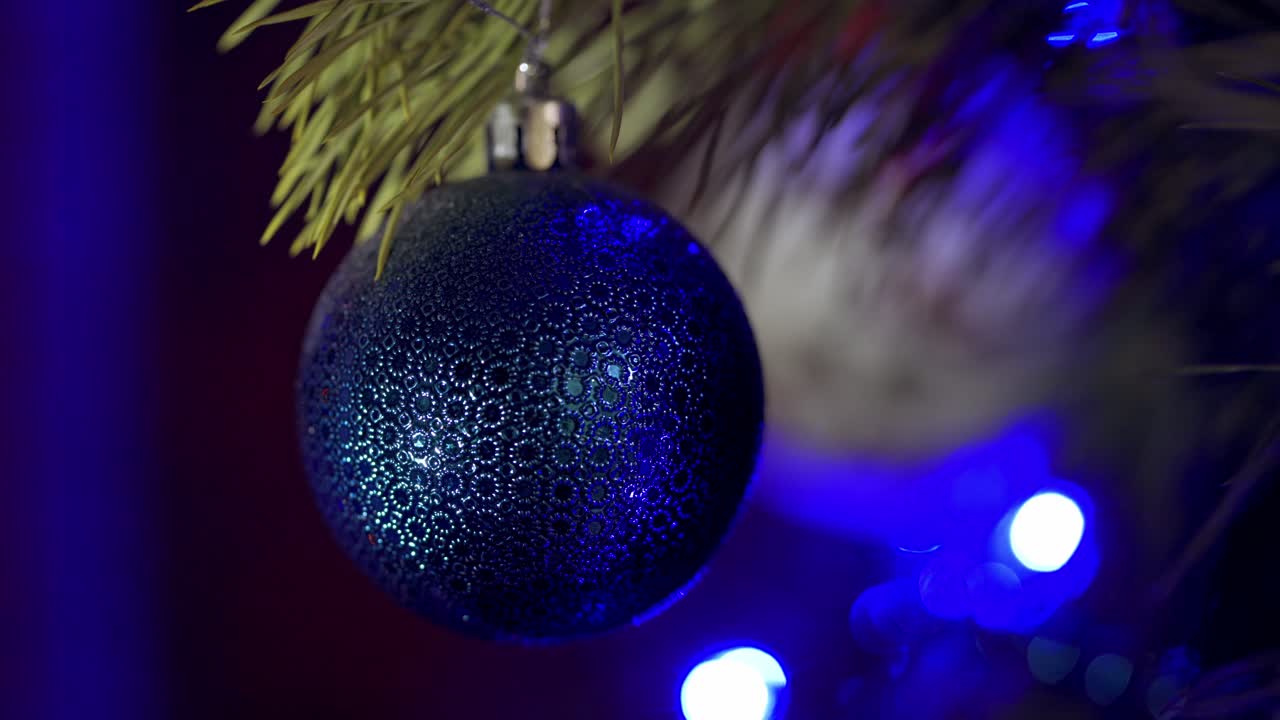 Big blue bauble on pine tree at Christmas. Christmas and New Year decoration. Christmas ball on the background of twinkling lights. Beautiful shiny Christmas toy on a spruce tree. Close-up.