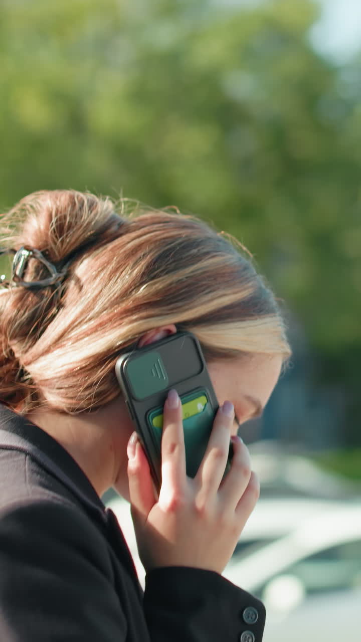 Signora elegante con un sorriso caloroso che parla al telefono con un socio in affari mentre esce da una riunione, ripresa attraverso la porta a vetri con uno sfondo urbano che riflette il paesaggio cittadino