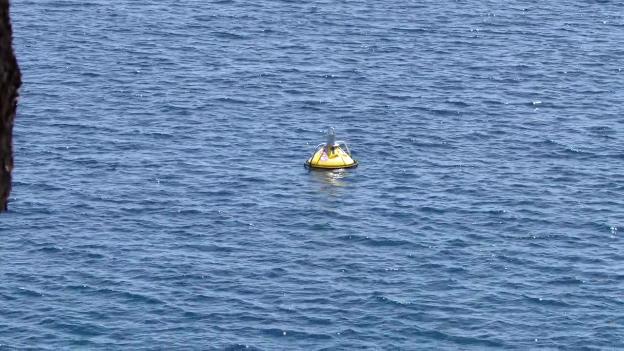 Static high angle shot of a yellow marker buoy bobbing on sparkling blue coastal water.