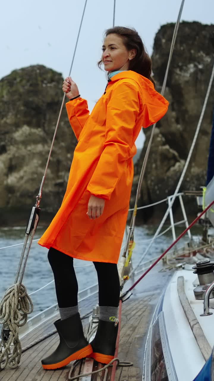 ผู้หญิงในเสื้อกันฝนสีส้มยืนอยู่บนดาดฟ้าเรือใบกลางทะเล