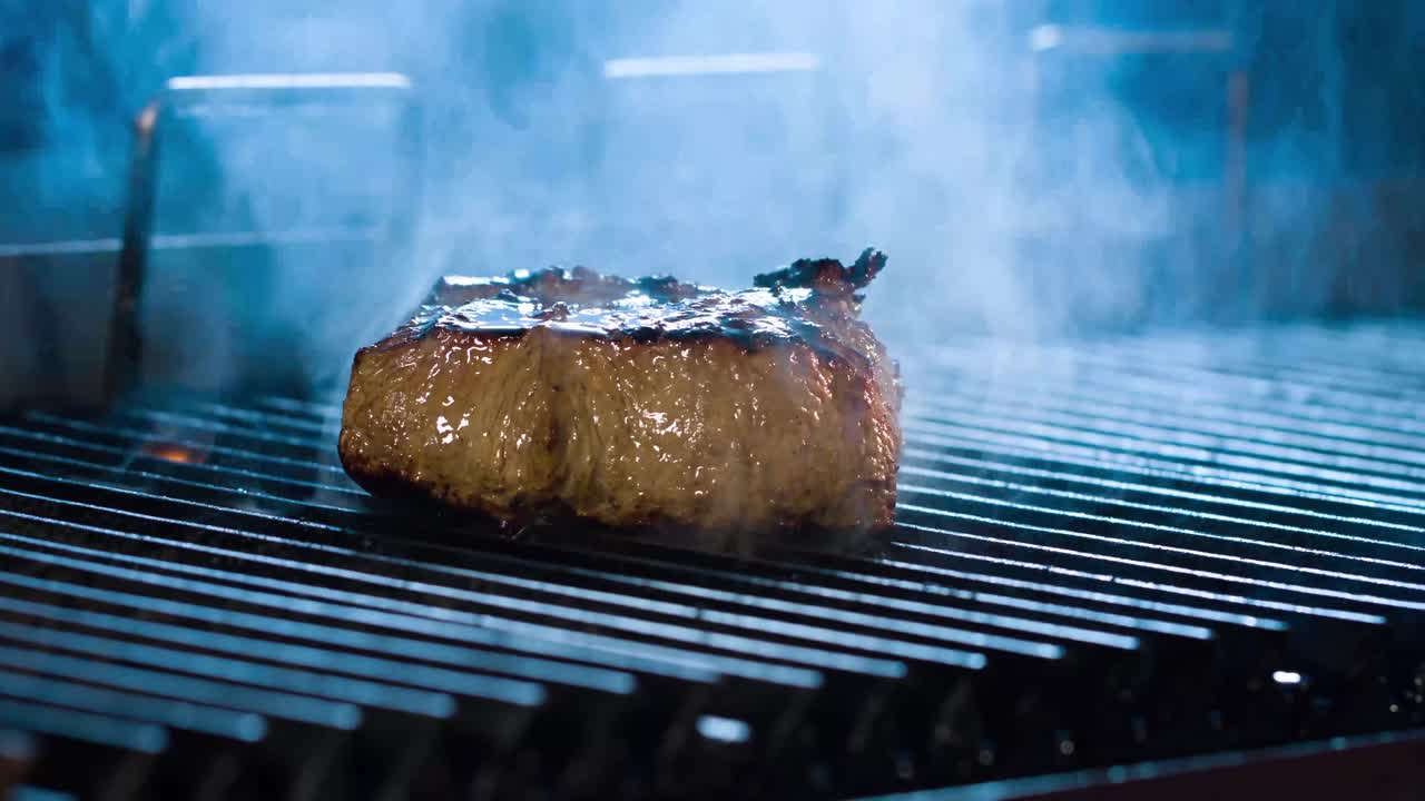 bistec grande a la parrilla, hay humo de las brasas a la carne, vista lateral, primer plano 4k bistec con una vista muy sabrosa 4k