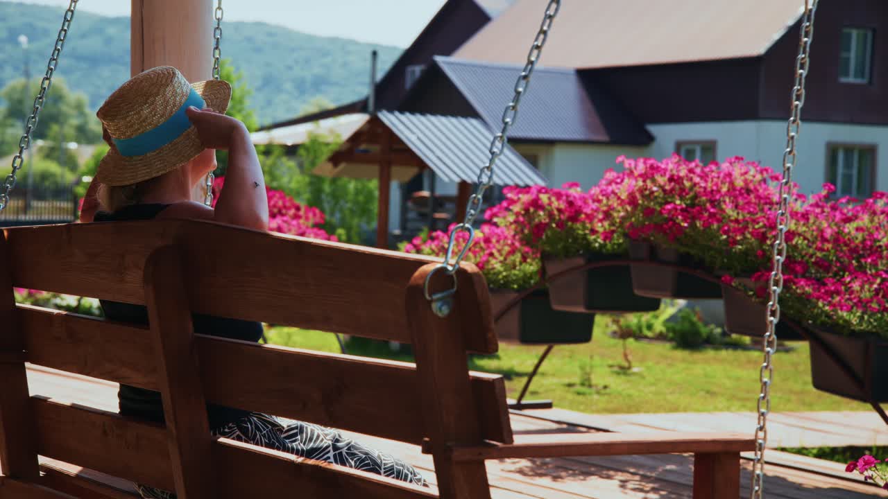 Woman in Straw Hat Relaxing on a Porch Swing in Summer