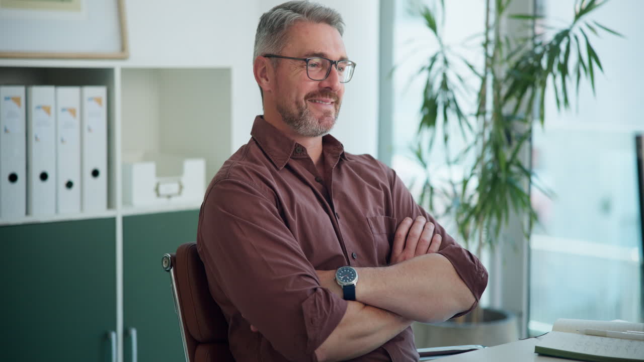 Midaldrende forretningsmand sidder og smiler på et moderne kontor.