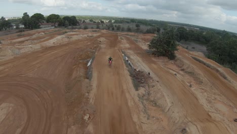 dos pilotos de motocross circulando por una pista de tierra en un día nublado mientras el tractor construye las rampas