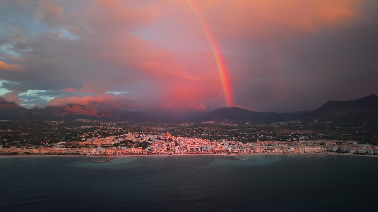 Arcobaleno vibrante si inarca su una città costiera al tramonto con montagne