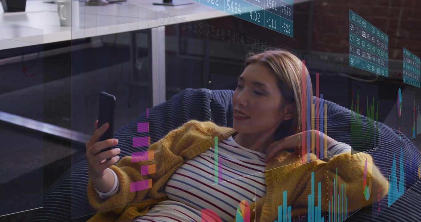 Remote worker in loft lounge lifting smartphone revealing floating financial data analyzing trends