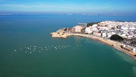 Sailboats-anchored-on-the-coastline-of-the-white-city-of-Cadiz,-Spain-aerial-view