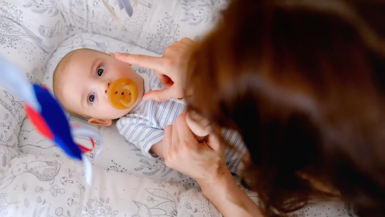 Cute little baby lying in the crib and mother putting pacifier in mouth 4k