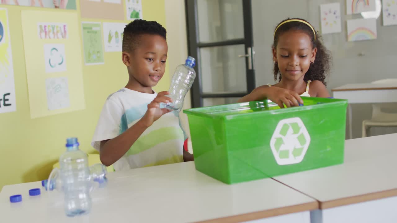 video de una feliz niña y un niño afroamericanos clasificando botellas de plástico para reciclar en el aula