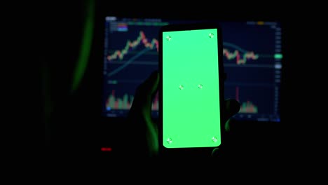 a trader holds a smartphone with a green screen in hands in a dark room. 4k