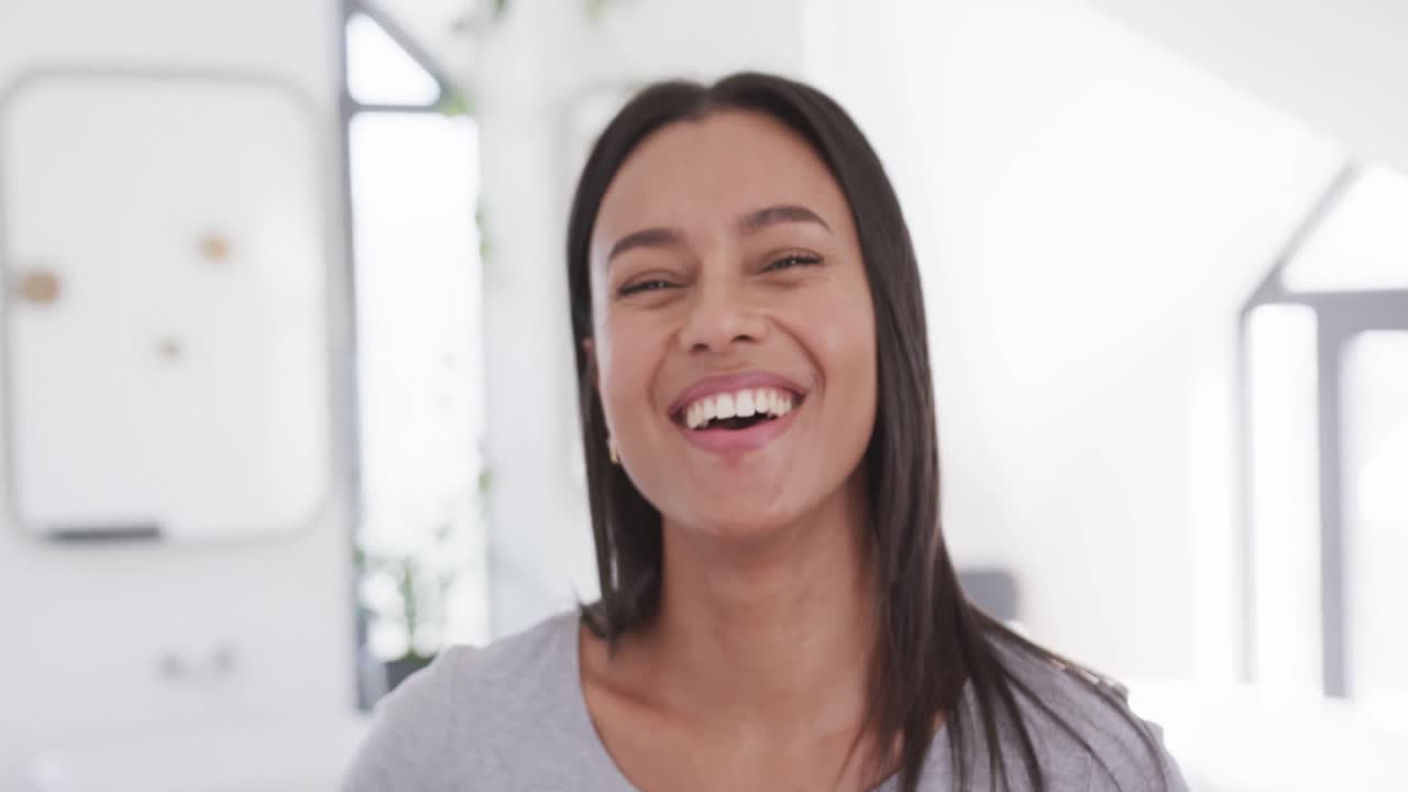 retrato de una feliz mujer biracial con cabello oscuro liso sonriendo en casa, en cámara lenta