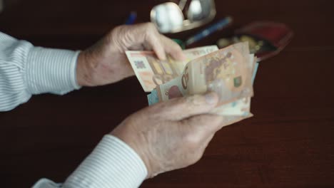 senior man counting monthly profit, wrinkled hands of old man counting and dividing 10, 20 and 50 euro banknotes at the desk table, concept of savings and making money