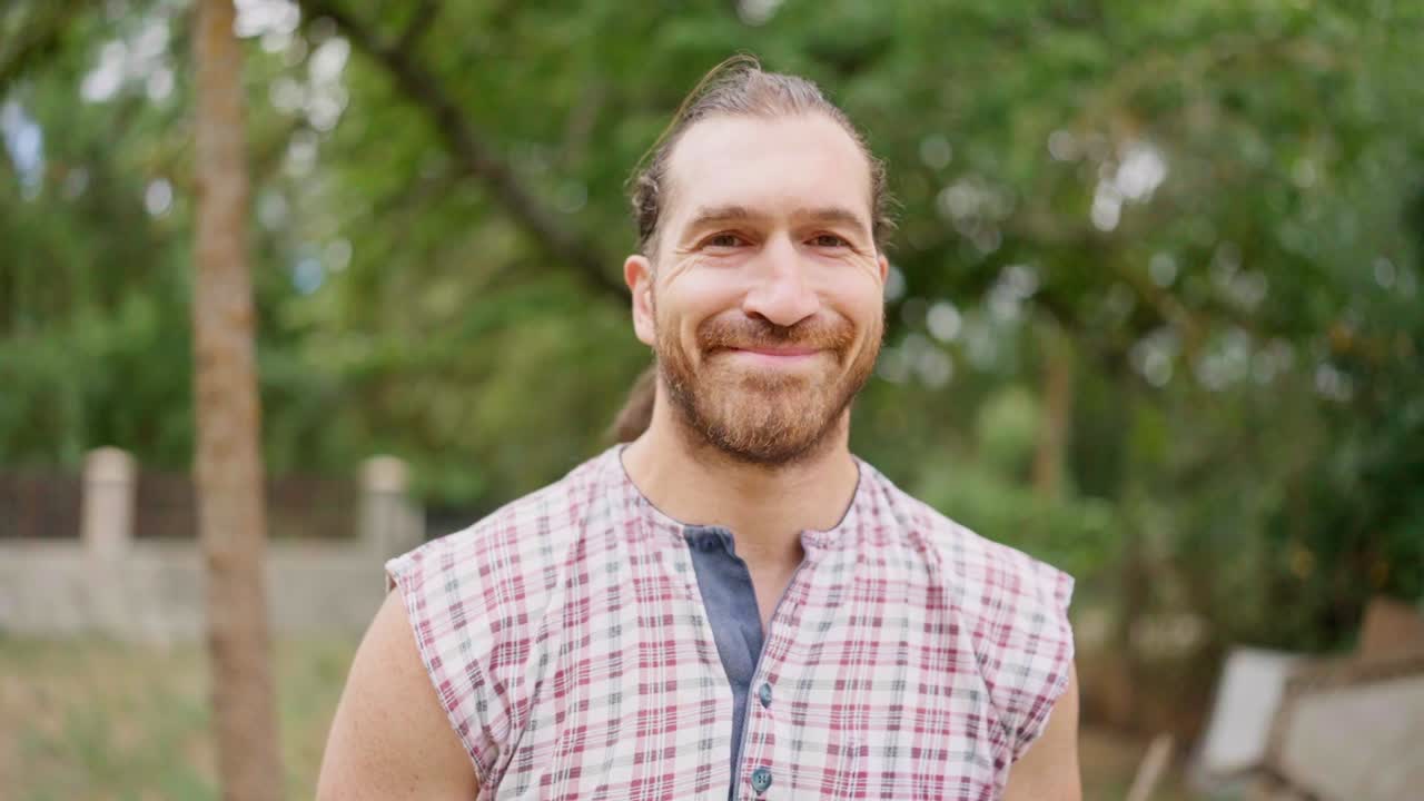 Smiling man with a beard and plaid shirt outdoors
