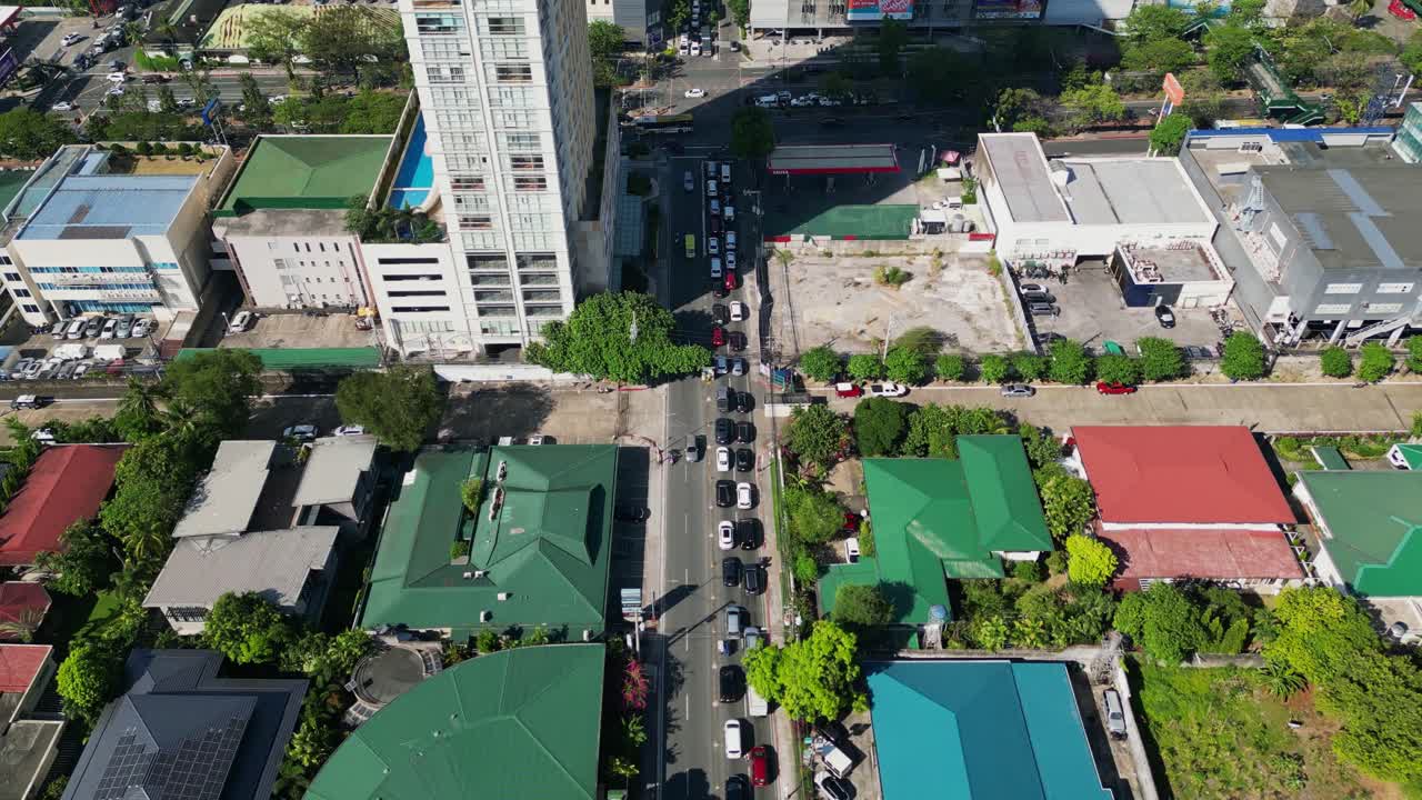 Overhead drone shot of cars waiting in traffic along Wilson Street, Greenhills with residential and commercial buildings during daytime - San Juan City, Philippines
