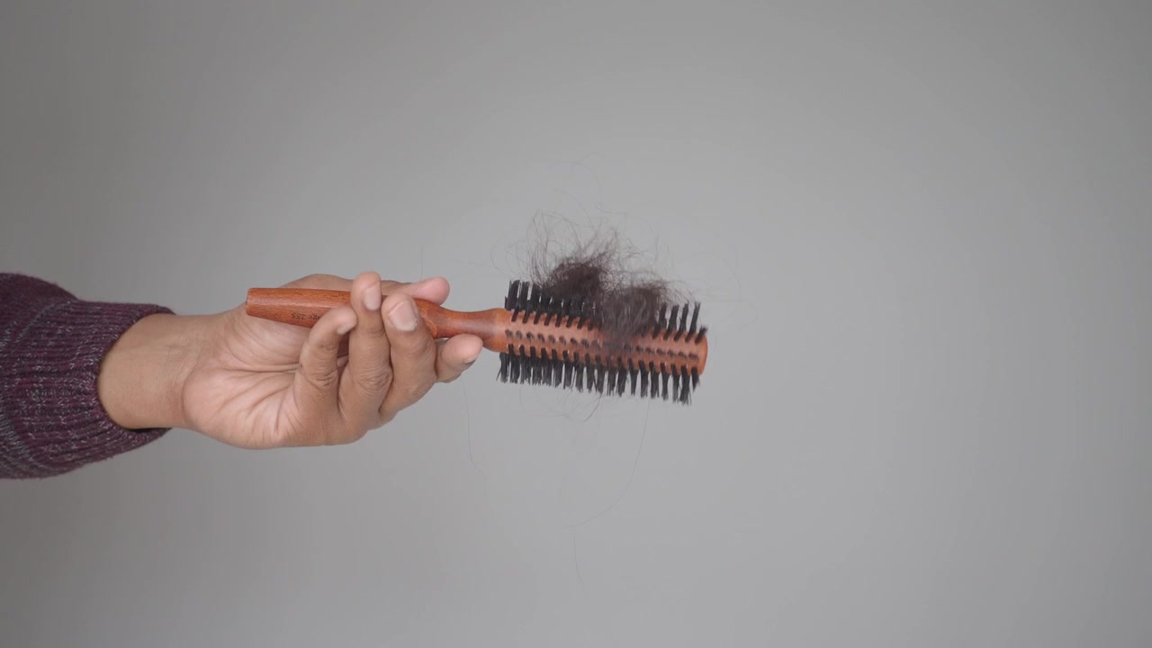 Tangan Memegang Sisir dengan Rambut Rontok yang Kusut