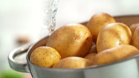 washing unpeeled potatoes in a colander under a stream of water splashing in slow motion