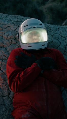 astronaut with helmet lying on a rock at night on a lifeless planet