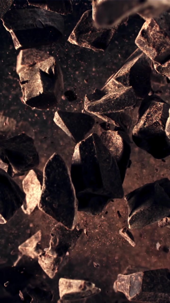 Trozos de chocolate negro cayendo a cámara lenta con cacao en polvo