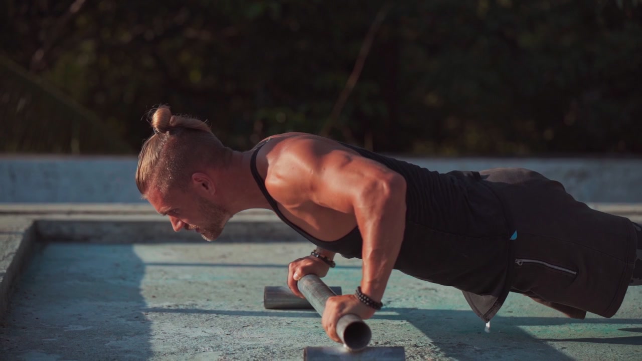 Muscular Man Performing Push-Ups on Metal Bars Outdoors