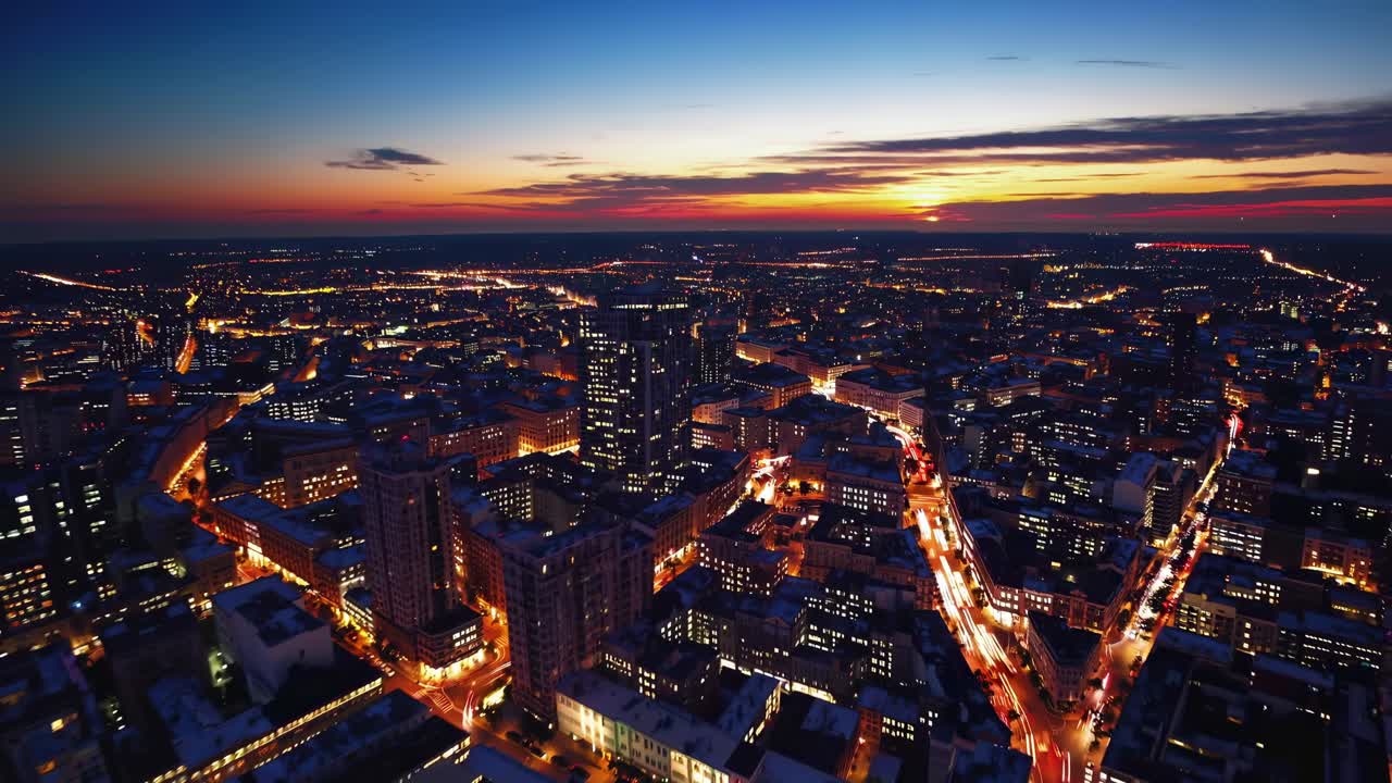 Aerial view of a cityscape at dusk, capturing vibrant lights and a colorful sunset