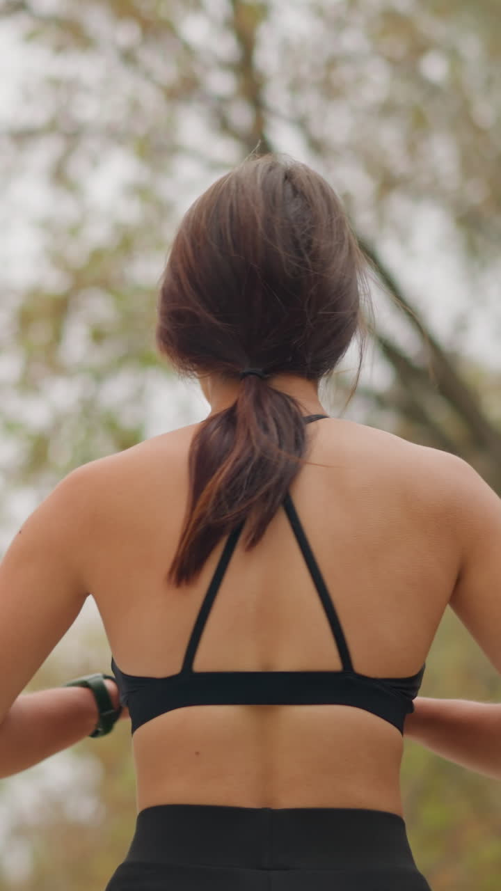 Close-up view of lady swinging her body under bright sunlight, outdoors in park with dry trees in the background, showing fitness exercise, stretching, and physical activity