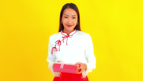 Pretty-Friendly-Asian-Woman-Presenting-a-Gift,-Yellow-Background-SLOMO