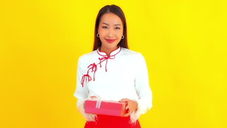 pretty friendly asian woman presenting a gift, yellow background slomo