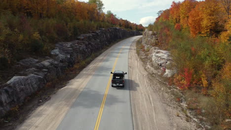 country road with pick up truck leading through autumn forest and rocky cliffs sides